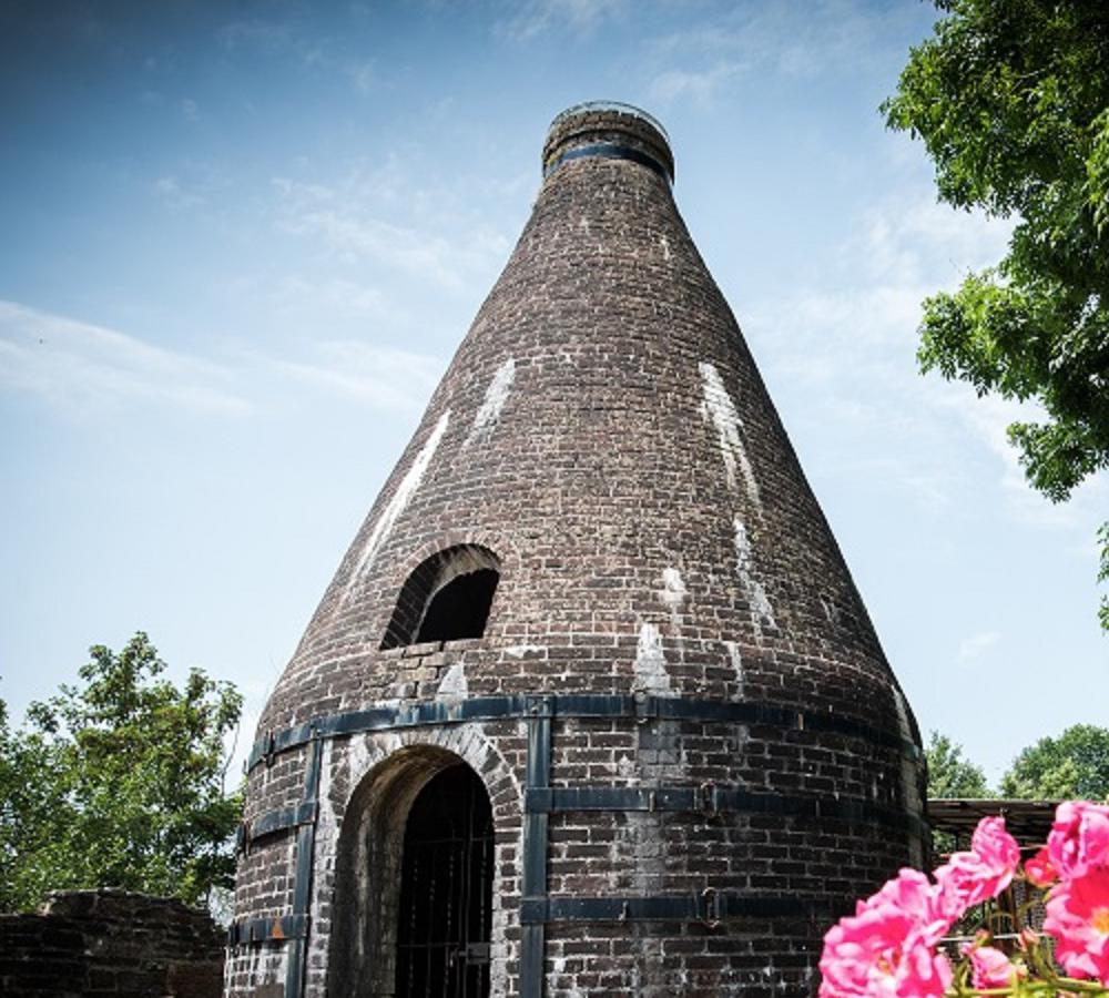 The original conical pottery  kiln at Nantgarw China Works Museum, surrounded by flowers and trees.